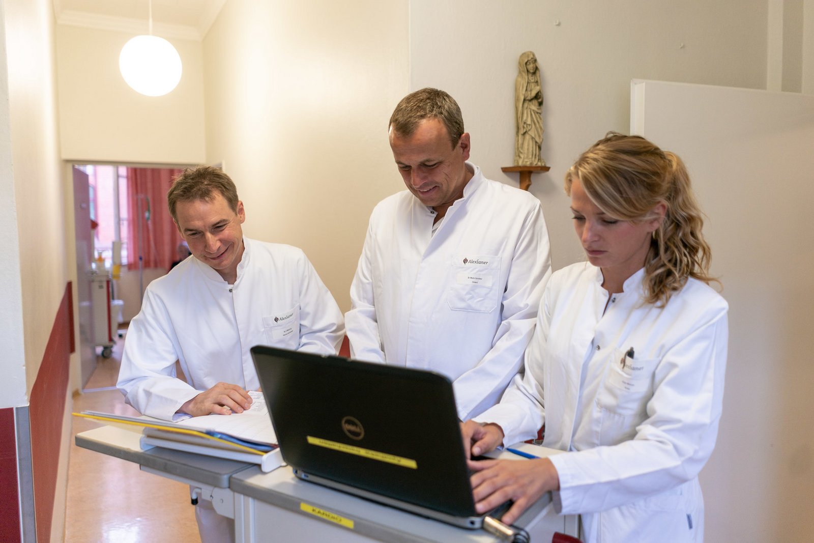Drei Fachärzt*innen stehen um einen mobilen Tisch und begutachten Daten.